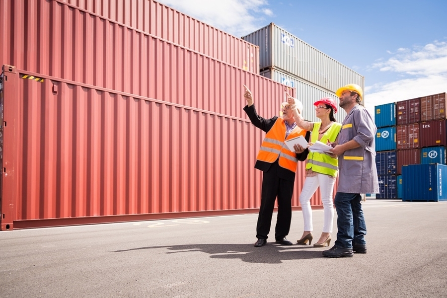 Three people with hard hats pointing in the air in front of cargo containers