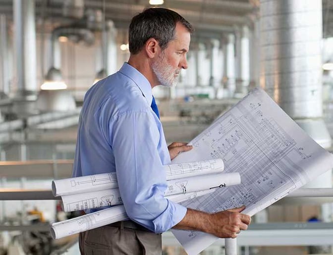 A man holds blueprints in a factory