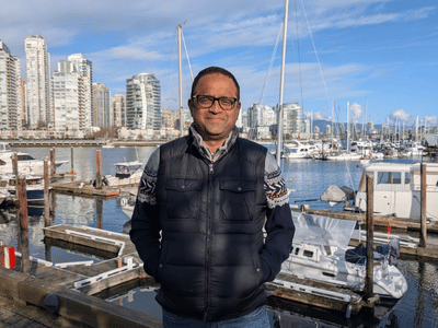 Badri Ratnam stands in front of a marina with buildings and water in the background.