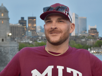 Joshua smiling and wearing a maroon MIT shirt and matching baseball cap