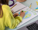 A child wearing a yellow sweater is drawing the planet Earth on a notebook. The word “Earth” is colored in green