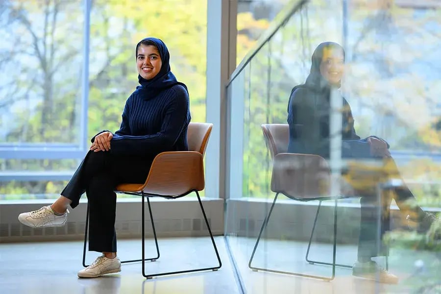 Sarah Alnegheimish sits in front of a wall of windows overlooking out-of-focus trees.