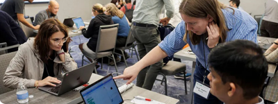 More than a dozen people sit around shared tables with laptops running App Inventor.