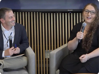 Photo of two adults in business clothes sitting on chairs and speaking into microphones.