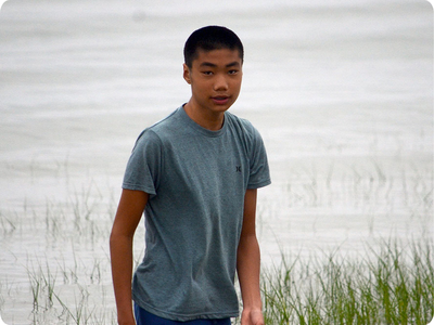 Teenager Dustin Liang standing in front of a lake with some tall grass in the foreground