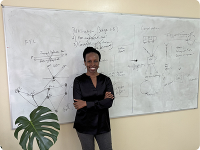 June Odongo poses in front of a whiteboard with writing on it.