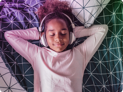 A kid relaxes while listening to headphones on their bed.