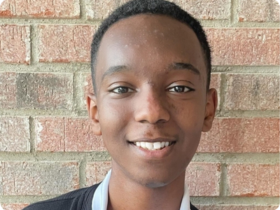 Portrait photo of Thomas Esayas, standing against a brick wall