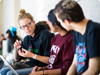 Photo of three college-aged students in conversation who are sitting with their computers on their laps.