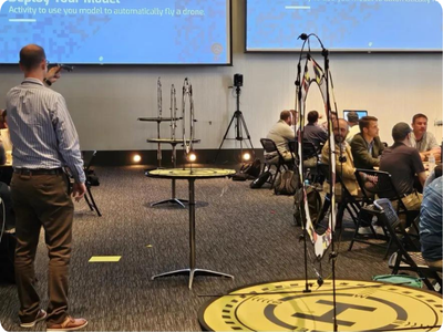 A group of people in a room with a projector are calibrating their drones to navigate targets.